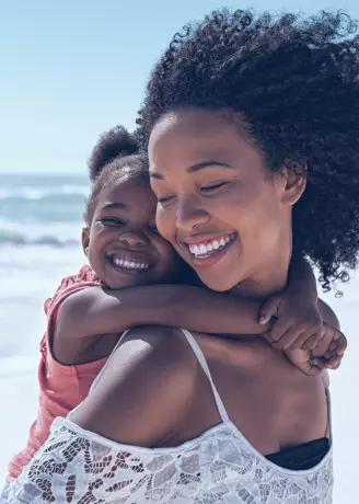 Imagem da mulher com sua filha abraçadas na praia.